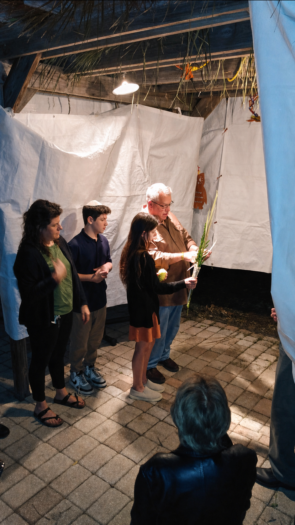 Students and family wave the lulav and etrog together in a Congregation Beth Shalom sukkah.